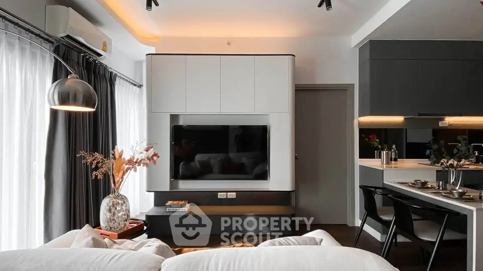 Modern living room with sleek design, featuring a wall-mounted TV, stylish decor, and open kitchen layout.