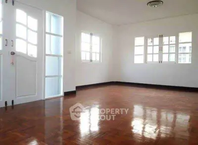 Spacious empty room with polished wooden floors and large windows.