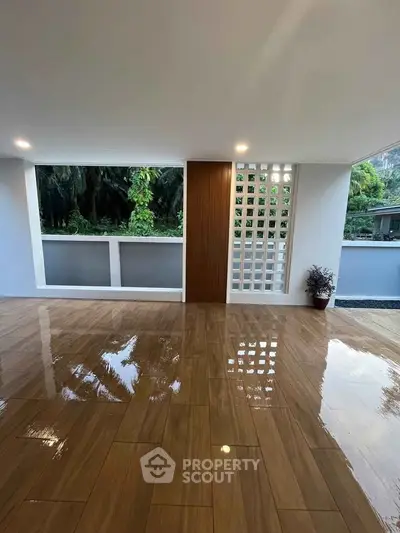 Spacious open area with glossy wooden flooring and lush greenery view.