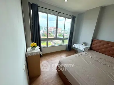Bright bedroom with large window offering city view, modern furnishings, and wooden flooring.