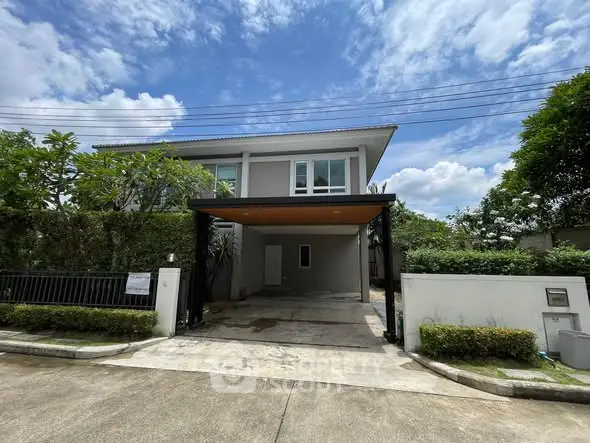 Modern two-story house with spacious driveway and lush greenery under a clear blue sky.