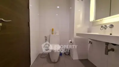 Modern bathroom with sleek fixtures and white tiles, featuring a toilet and a contemporary sink.