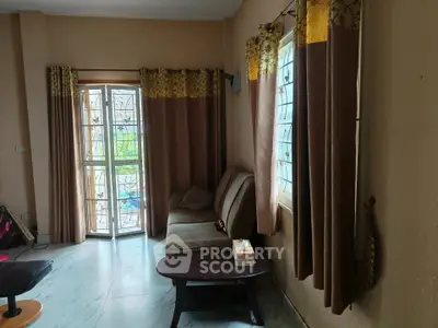 Cozy living room with sofa, curtains, and natural light through large windows.