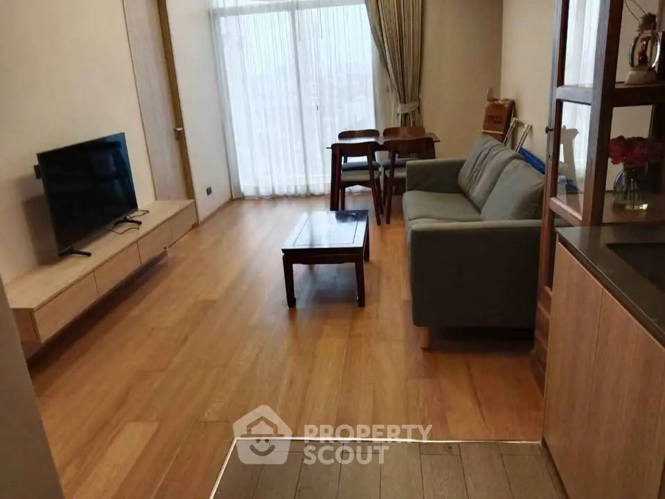Modern living room with wooden flooring, sleek furniture, and natural light from large windows.