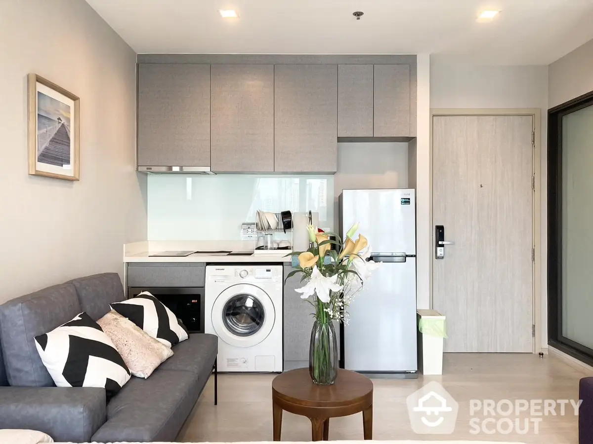 Modern studio apartment with integrated living space, featuring sleek kitchen cabinetry, stainless steel appliances, and a cozy sitting area.