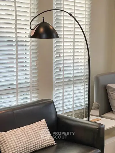 Modern living room with stylish black leather sofa and elegant floor lamp by large windows.