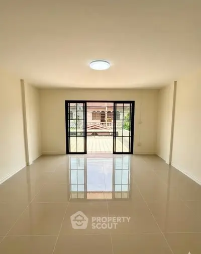 Spacious living room with large windows and tiled flooring, offering ample natural light and a serene view.
