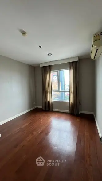 Spacious empty room with wooden flooring and large window in modern apartment.