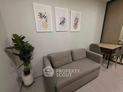 Modern living room with stylish gray sofa, plant, and wall art in a cozy apartment setting.