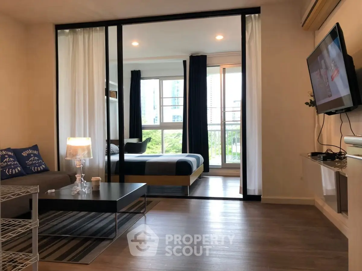 Modern open-plan living room with stylish decor and a view into a cozy bedroom.