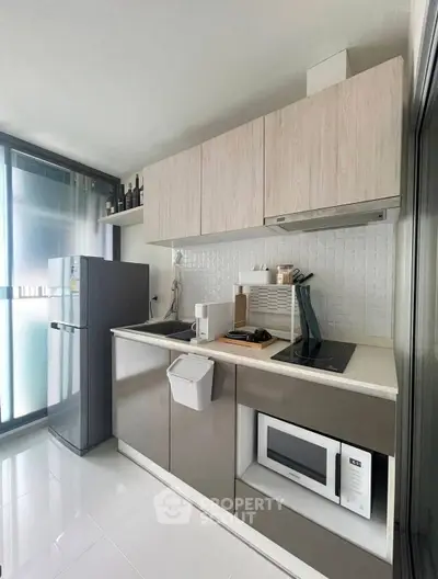 Modern kitchen with sleek cabinetry, built-in microwave, and compact fridge in a stylish apartment.