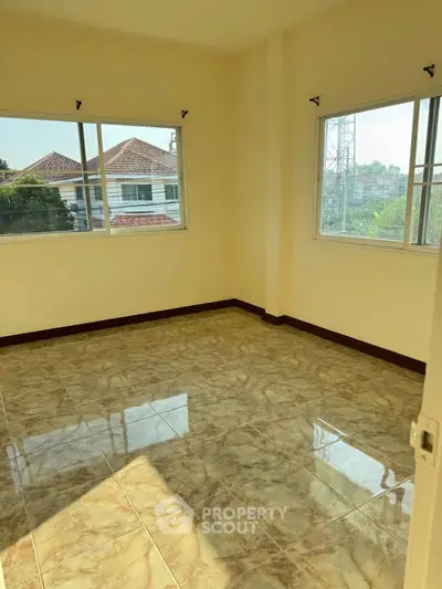 Bright empty room with tiled floor and large windows offering a sunny view.