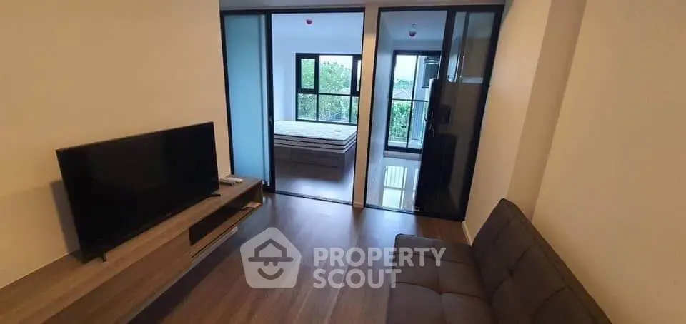 Modern living room with sleek furniture and large windows offering natural light and a view of greenery.