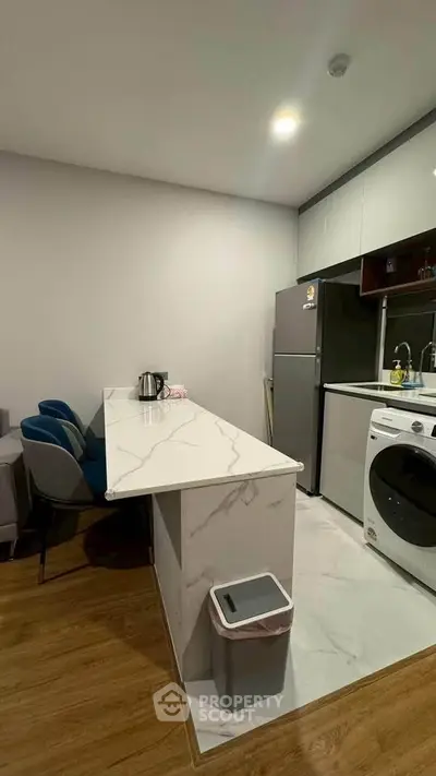 Modern kitchen with marble countertop, washing machine, and sleek appliances in a cozy apartment.