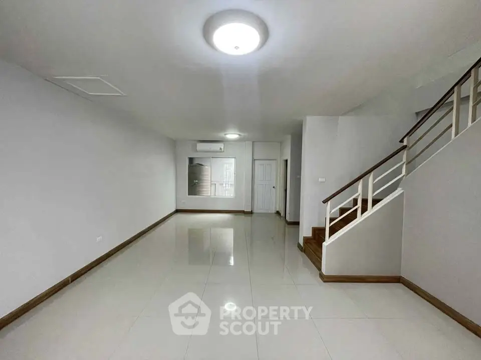 Spacious modern living room with sleek staircase and polished tile flooring.