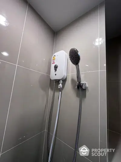 Sleek modern bathroom with wall-mounted electric shower unit and adjustable shower head, featuring glossy neutral-toned tiles.