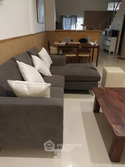 Spacious living room with modern gray sofa and elegant wooden dining set, perfect for family gatherings.