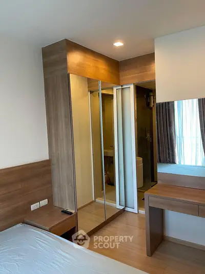 Modern bedroom with mirrored closet and wooden furniture, featuring a glimpse of an ensuite bathroom.