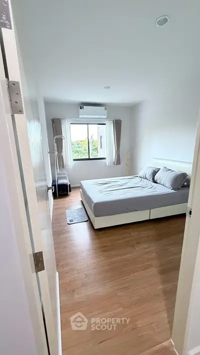 Spacious bedroom with modern decor and large window offering natural light.