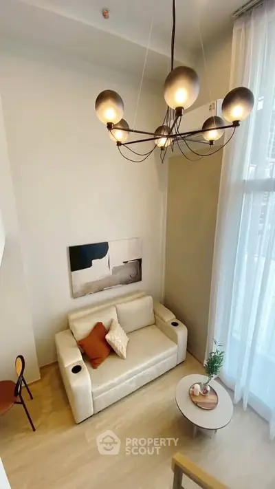 Modern living room with high ceiling, elegant chandelier, and cozy seating area in a stylish apartment.