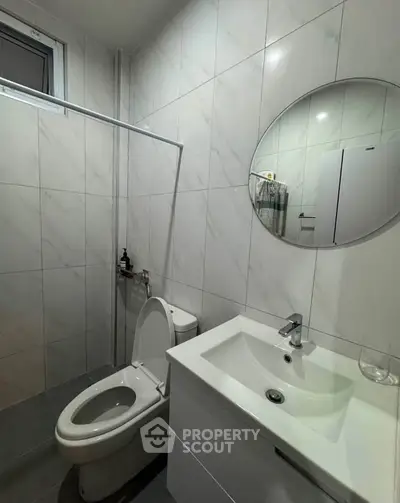 Modern bathroom with sleek white fixtures and round mirror, featuring elegant tile design.