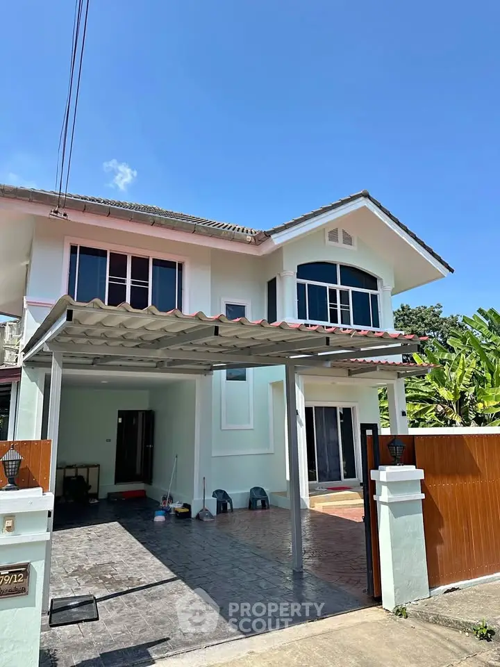 Charming two-story house with carport and lush greenery, perfect for family living.
