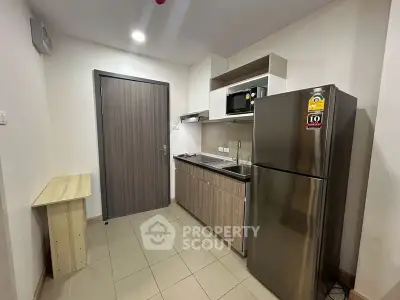 Modern compact kitchen with stainless steel fridge and microwave in cozy apartment.