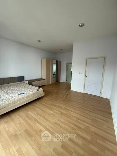 Spacious bedroom with wooden flooring and modern furniture in a bright apartment.
