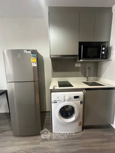 Modern kitchen with sleek appliances including fridge, washing machine, and microwave in compact layout.