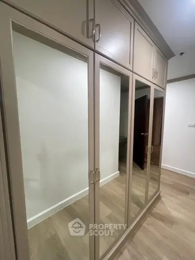Elegant bedroom with large mirrored wardrobe doors reflecting a spacious interior, featuring high-quality wooden flooring and tasteful neutral decor.