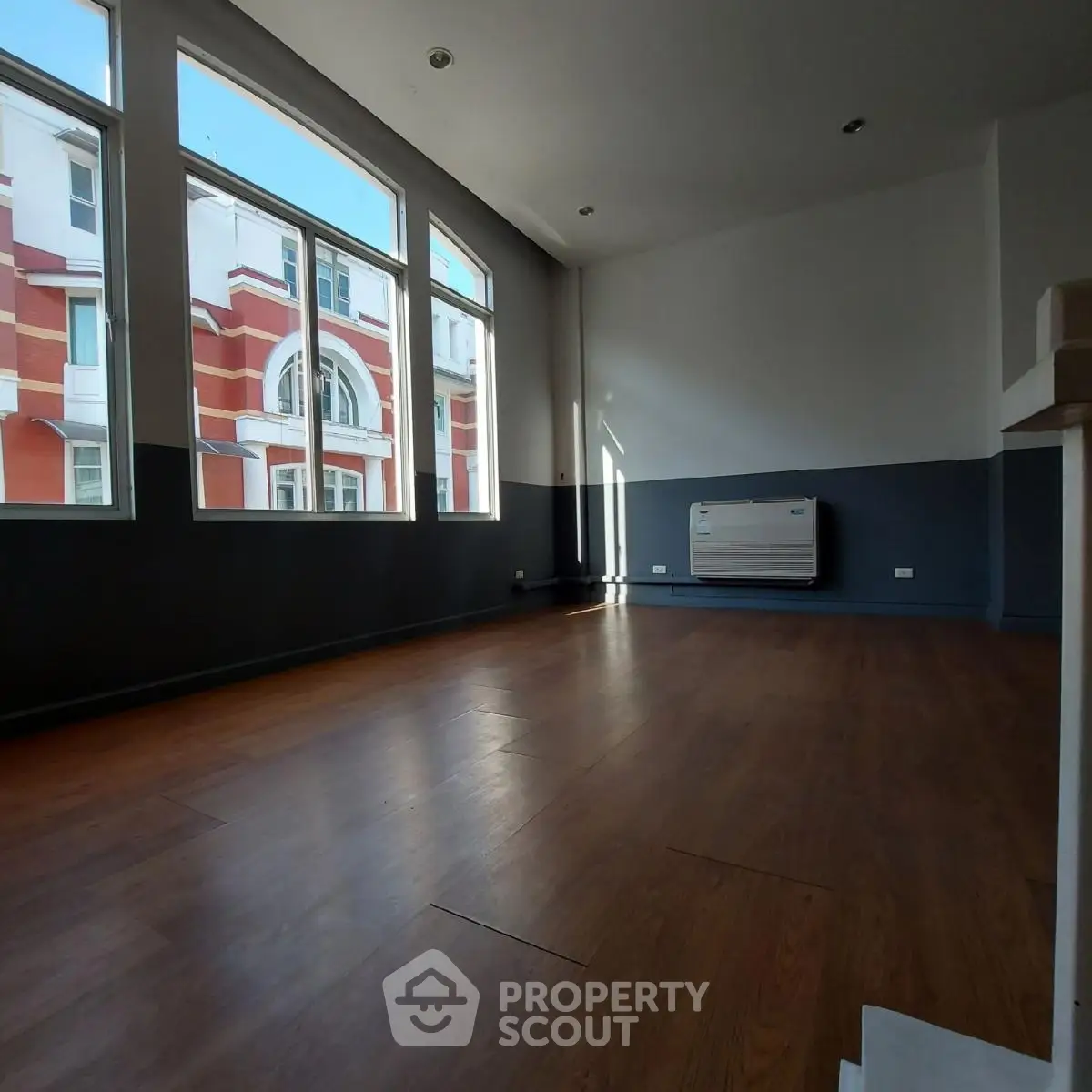 Spacious room with large windows and wooden flooring, ideal for modern living.