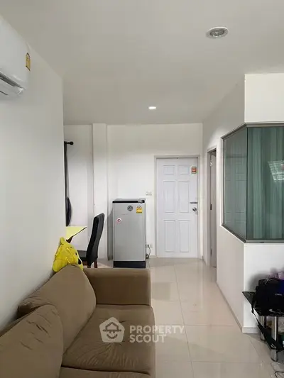 Modern living room with beige sofa, compact fridge, and sleek white interiors.
