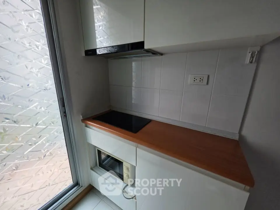 Compact kitchen with electric stove and oven, featuring modern white cabinetry and frosted glass window.