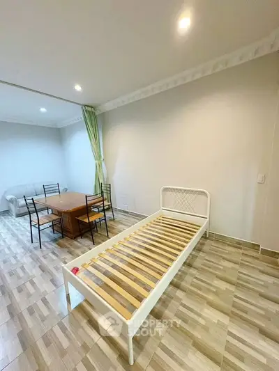 Spacious living area with dining set and single bed, featuring modern tile flooring and recessed lighting.