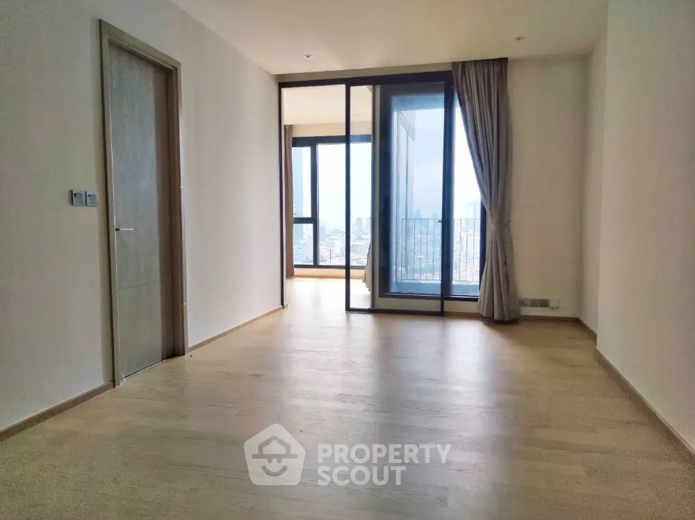 Spacious empty room with wooden flooring and large windows offering city view