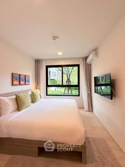 Spacious bedroom with large window and modern decor in a serene setting.