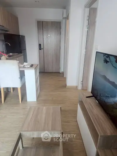 Modern living room with wooden flooring, sleek furniture, and a flat-screen TV, leading to a stylish kitchen area.