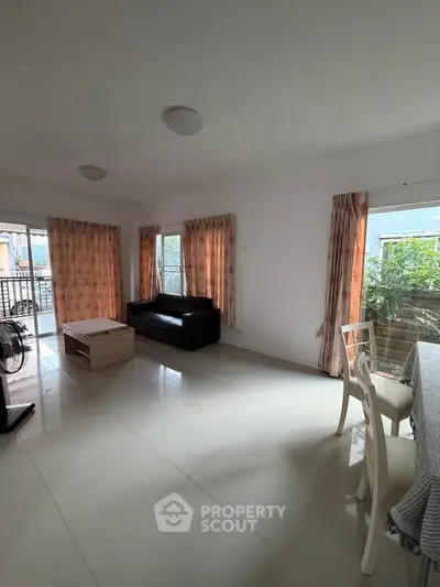 Spacious living room with large windows and balcony access, featuring modern furniture and natural light.