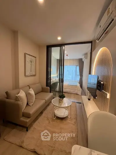 Modern living room with cozy sofa, stylish decor, and a view into the bedroom through glass doors.