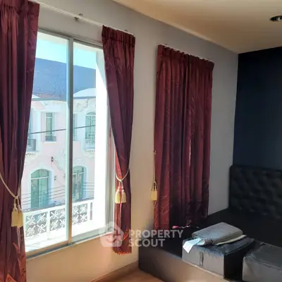 Charming interior with elegant curtains and a cozy seating area, offering a glimpse of classic architecture outside.