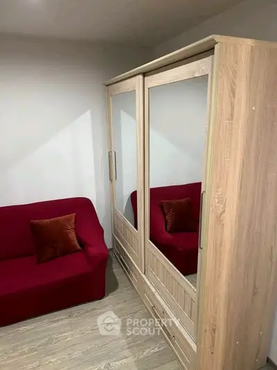 Cozy bedroom with mirrored wardrobe and red sofa, perfect for stylish living.