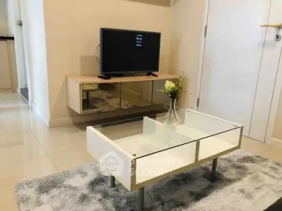 Modern living room with sleek TV stand and glass coffee table on plush rug.