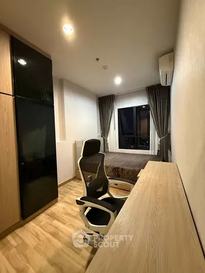 Modern bedroom with sleek furniture and city view, featuring a comfortable chair and stylish desk.
