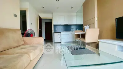 Modern living room with beige sofa, glass coffee table, and sleek kitchen area in open layout apartment.