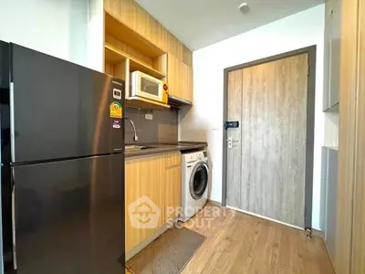 Modern compact kitchen with wooden cabinets, fridge, microwave, and washing machine.