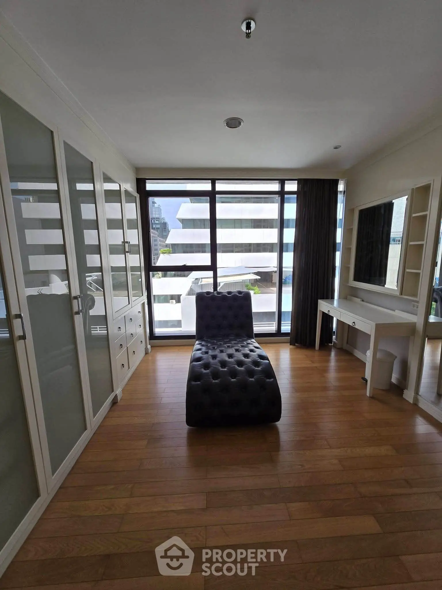 Spacious modern bedroom with large windows and stylish furniture in urban apartment.