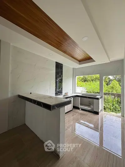 Modern kitchen with sleek marble countertops and large windows offering lush garden views.