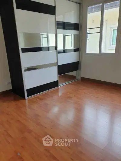 Spacious bedroom with wooden flooring and large mirrored wardrobe in modern apartment.