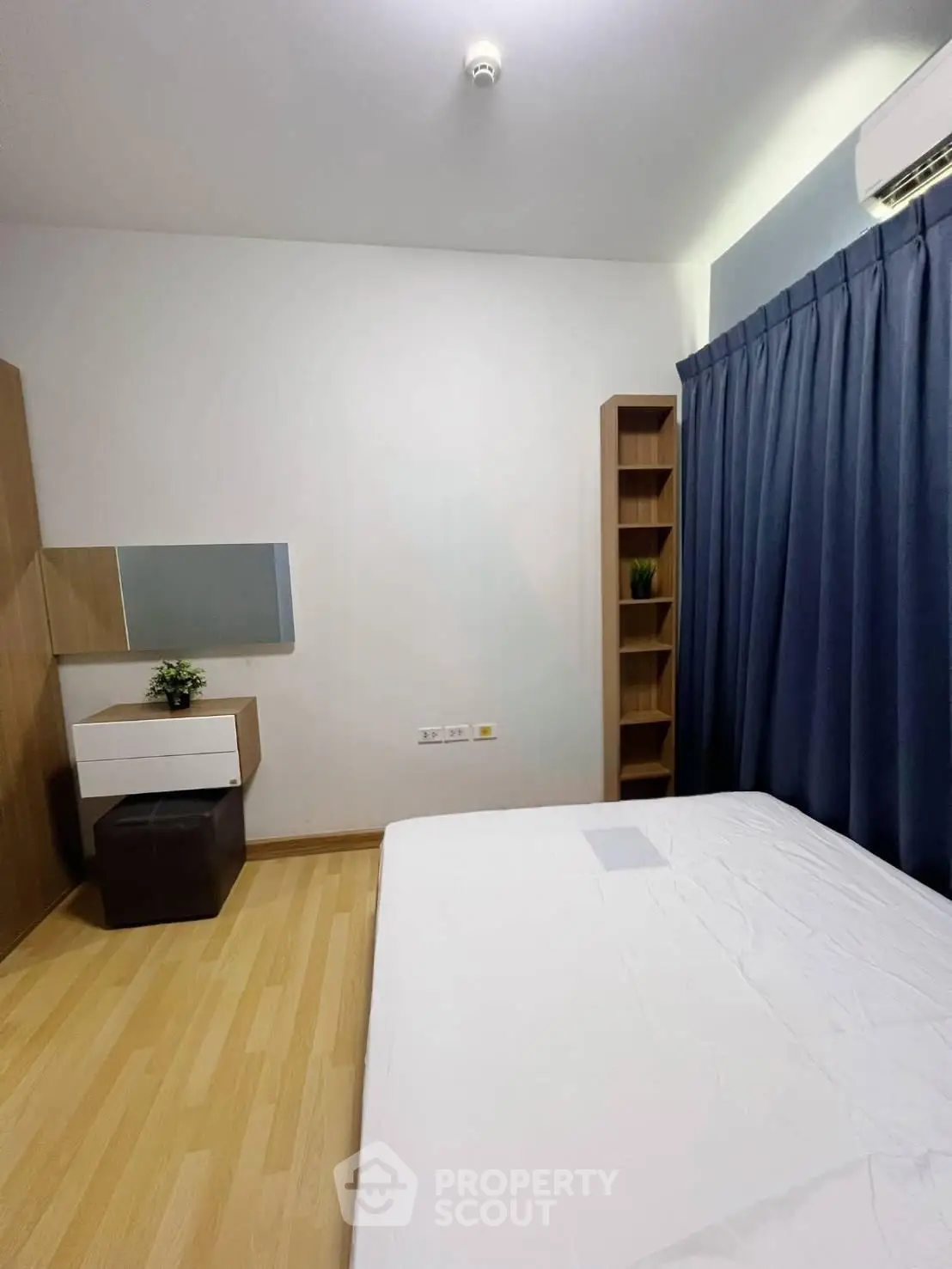 Modern bedroom with minimalist design, featuring wooden flooring, sleek furniture, and a large window with blue curtains.