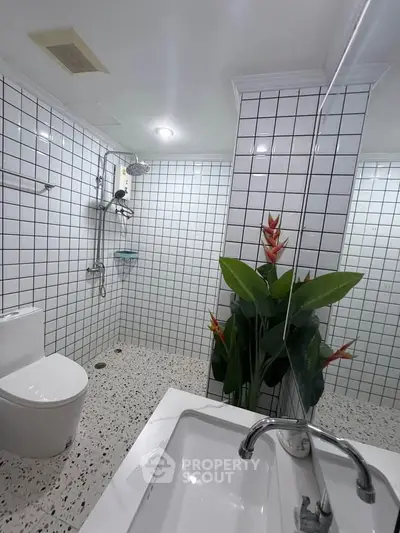 Modern bathroom with white tiles, sleek fixtures, and decorative plant for a fresh, contemporary look.